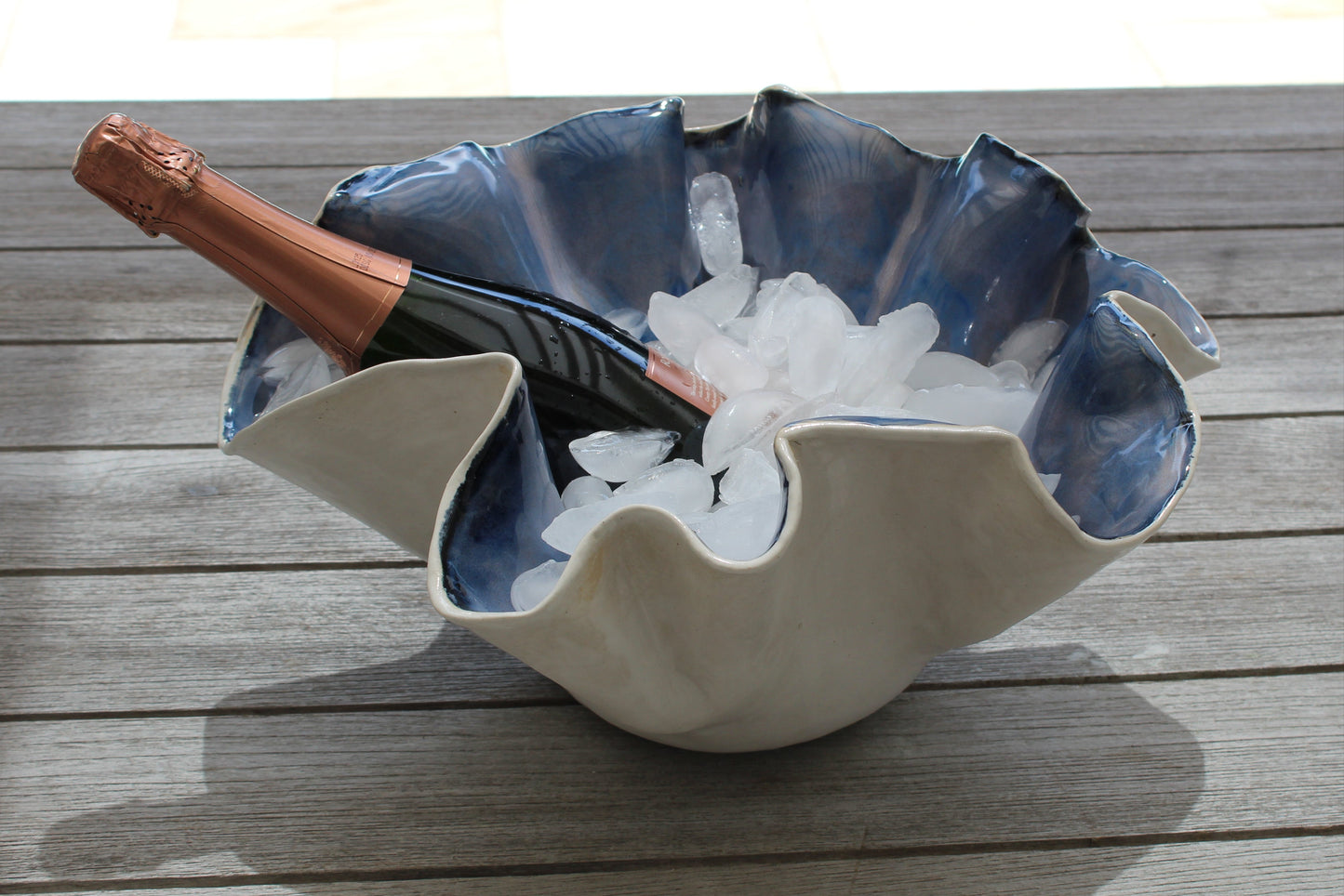 Shell-shaped ice bucket with a bottle of champagne on a wooden surface