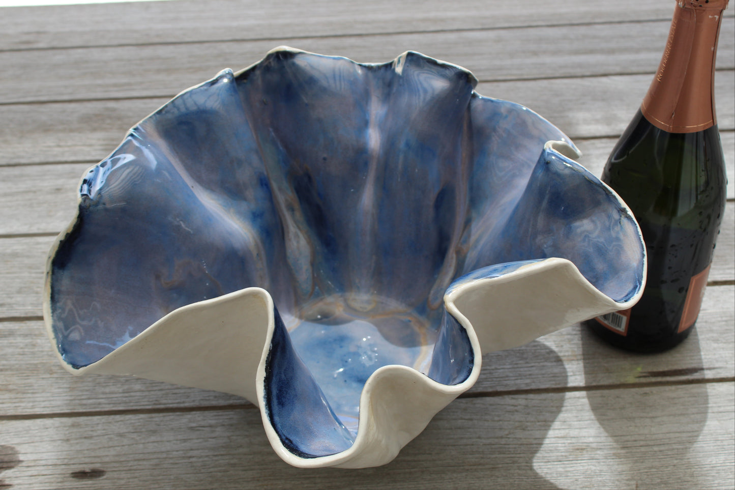 Blue and white ceramic shell-shaped bowl on a wooden surface with a bottle of champagne.